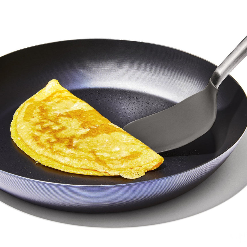 Folded yellow omelette in a black frying pan with a spatula.