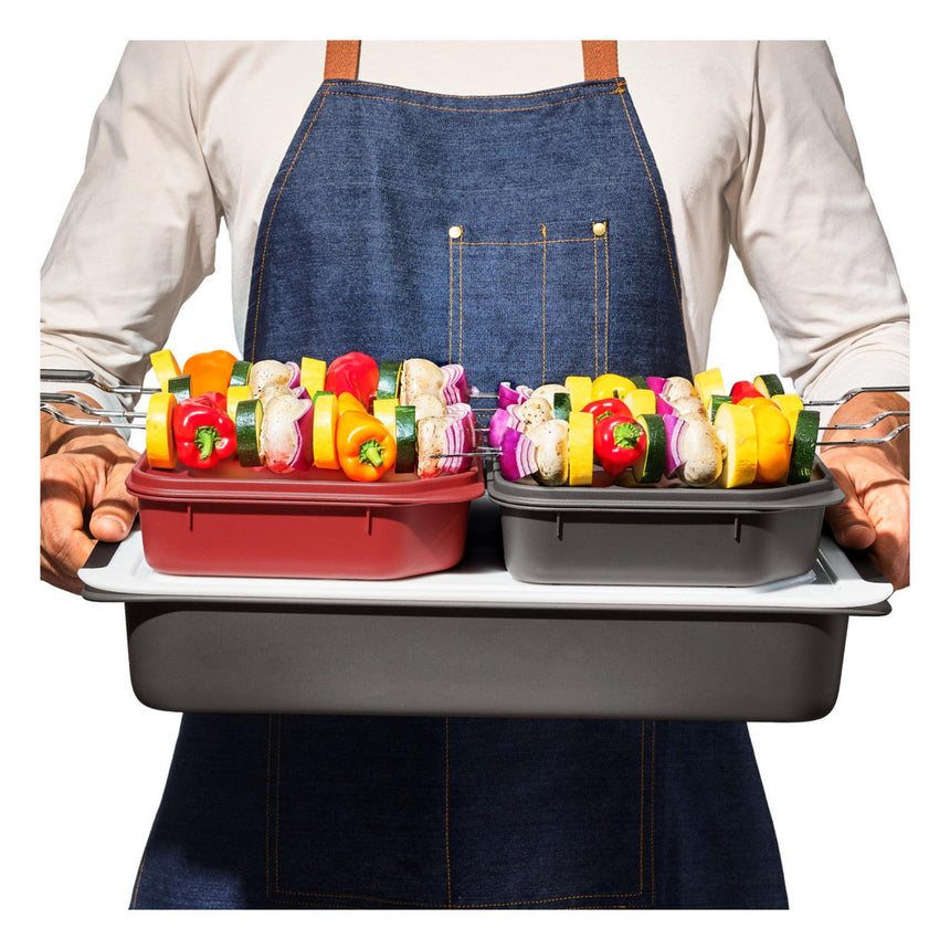 Person wearing a denim apron holding a tray with colorful bell peppers in containers.