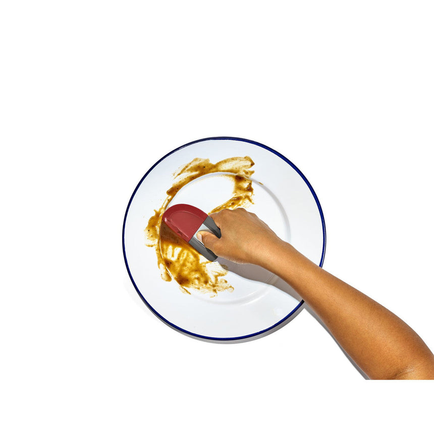 White plate with a blue rim containing a smear of yellow sauce and a hand holding a red-tipped utensil.