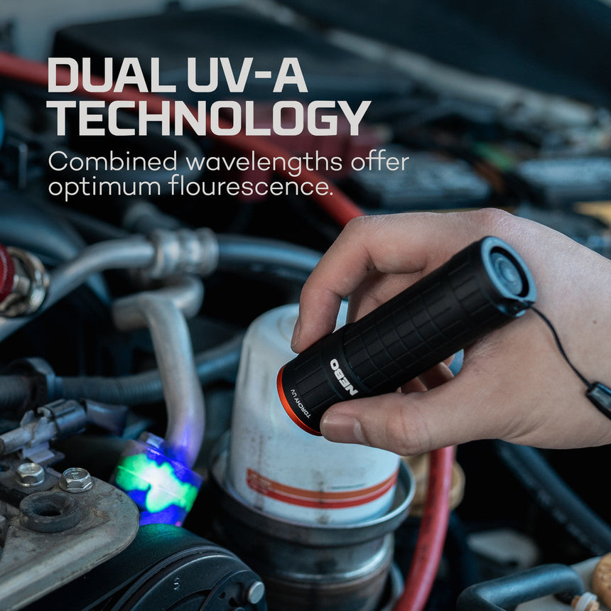 Handheld UV light device emitting blue illumination over an engine compartment.