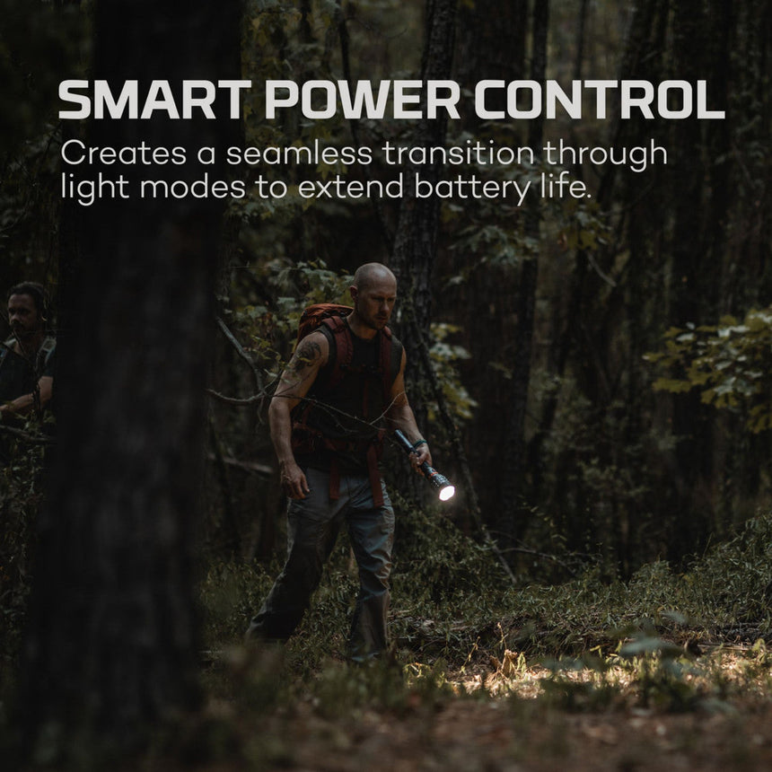 Person hiking in a dark forest while using a flashlight.