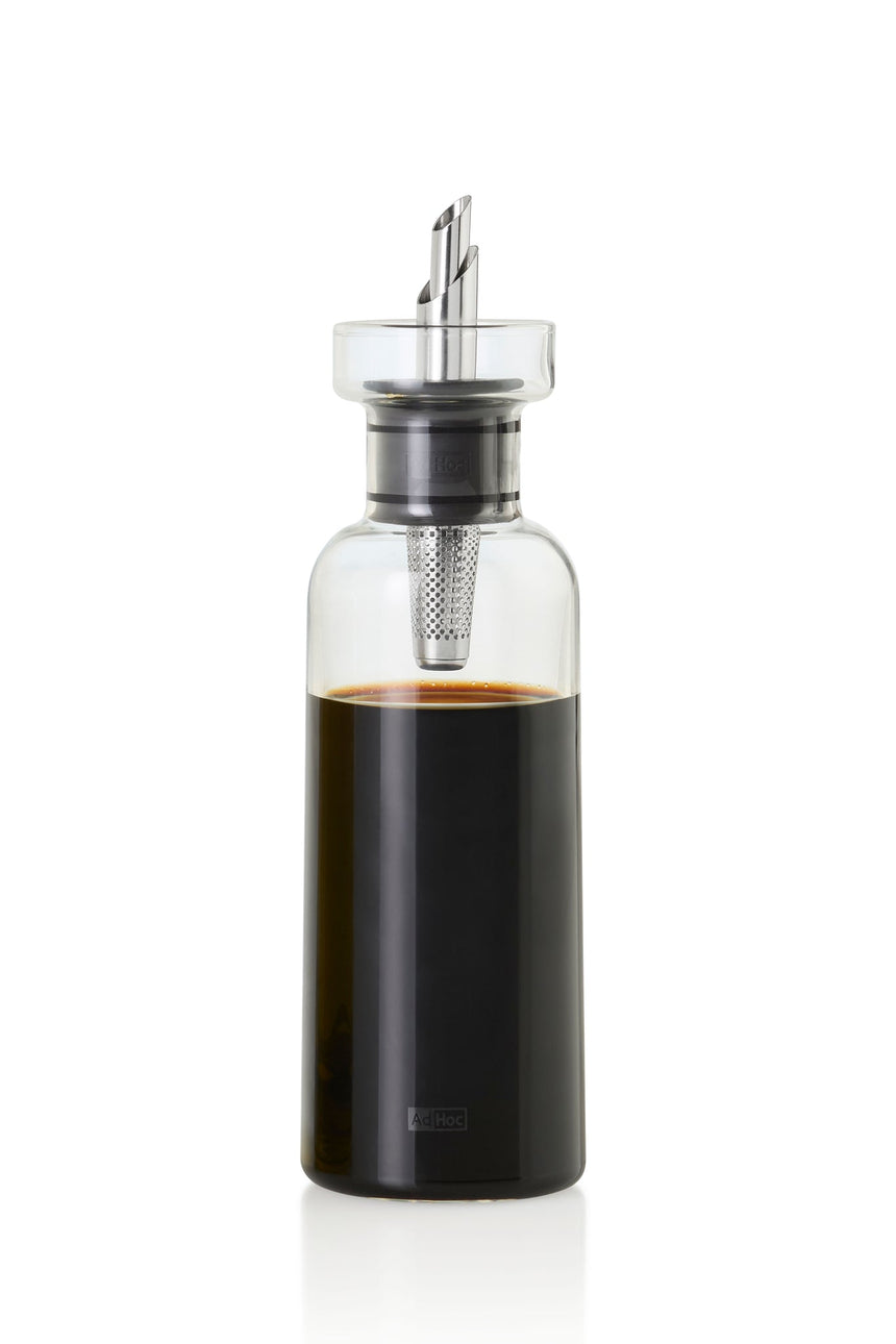 Glass bottle containing dark liquid with a metal and plastic pouring spout.