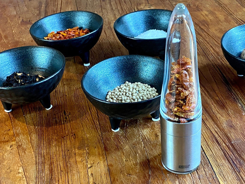 Electric spice or pepper grinder alongside several small blue bowls containing various spices or seasonings.