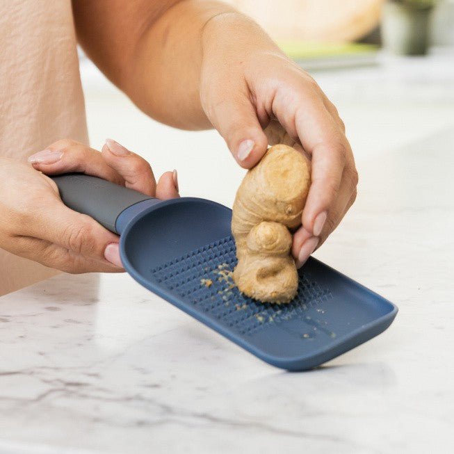 Ginger root being grated on a blue plastic grater.