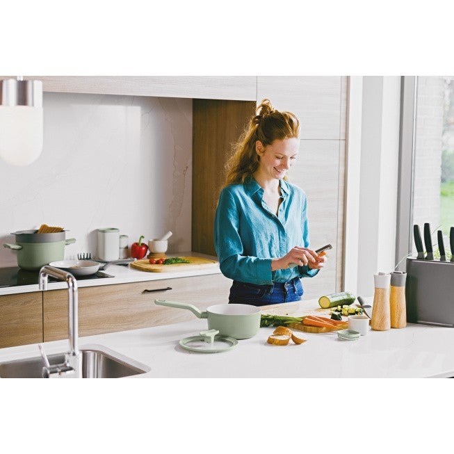 Woman in a blue shirt using a smartphone while standing in a kitchen.