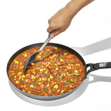 Frying pan filled with a colorful vegetable and meat stew or chili being stirred with a spoon.
