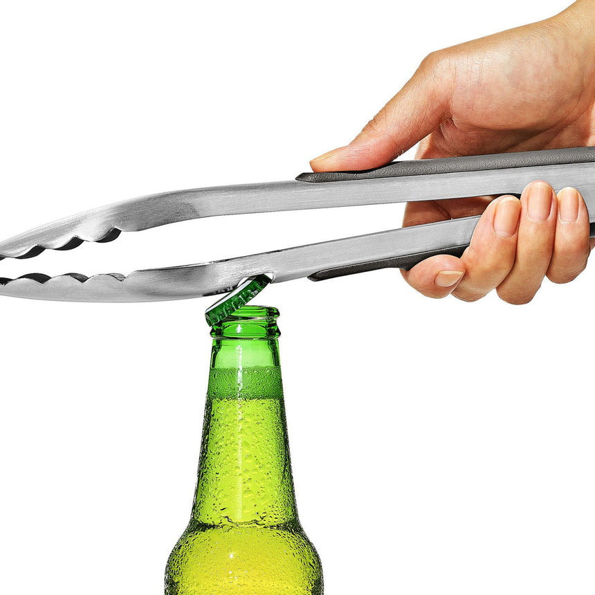 Stainless steel bottle opener tongs positioned to open a green glass beer bottle.