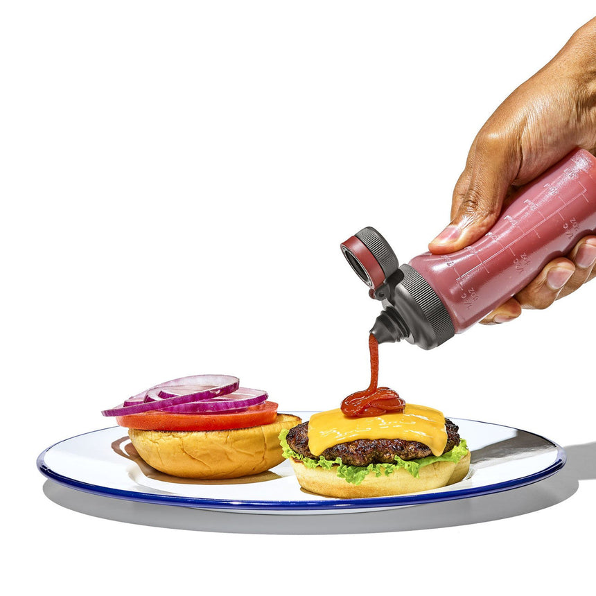 Hamburger on a plate with condiments being added from a squeeze bottle.