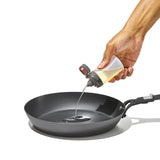 Non-stick frying pan with oil being poured into it from a squeeze bottle.