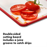 Double-sided cutting board with a red border and juice groove, displaying sliced tomatoes.