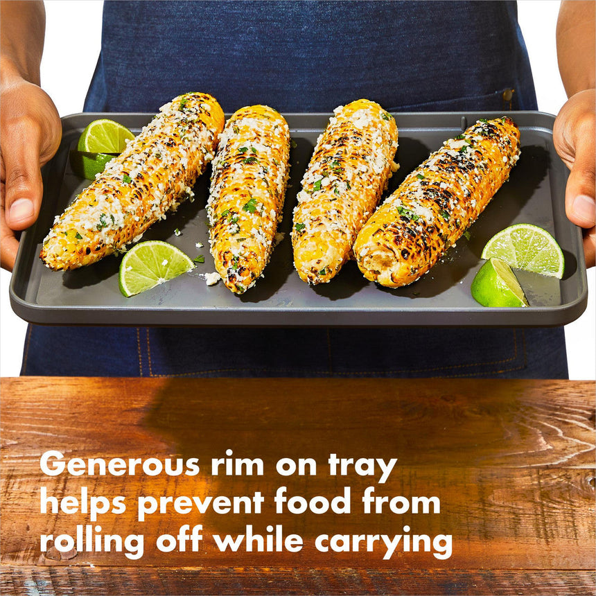 Four grilled corn cobs topped with seasonings and served with lime wedges on a metal tray.