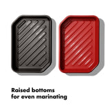 Two rectangular marinating trays with raised ridged bottoms, one black and one red.