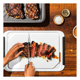 Grilled steak being sliced on a white cutting board.