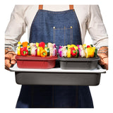 Person wearing a denim apron holding a tray with colorful bell peppers in containers.