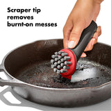 Scraper tool with a red handle and metal bristles for cleaning cookware.
