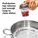 Dish scrubber brush with a soap-dispensing push-button top.