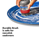 Dish scrubbing brush with red grip and gray bristles being used on a blue plate.