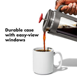 French press coffee maker pouring coffee into a white mug.