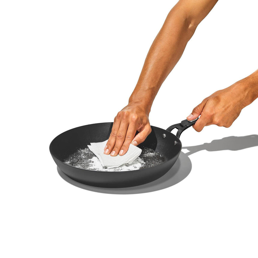 Non-stick frying pan with hands cleaning it using a sponge.