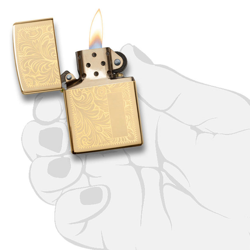 Gold-colored Zippo lighter with an ornate floral pattern, open and lit.