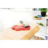 Raw steak with a meat tenderizer on top.