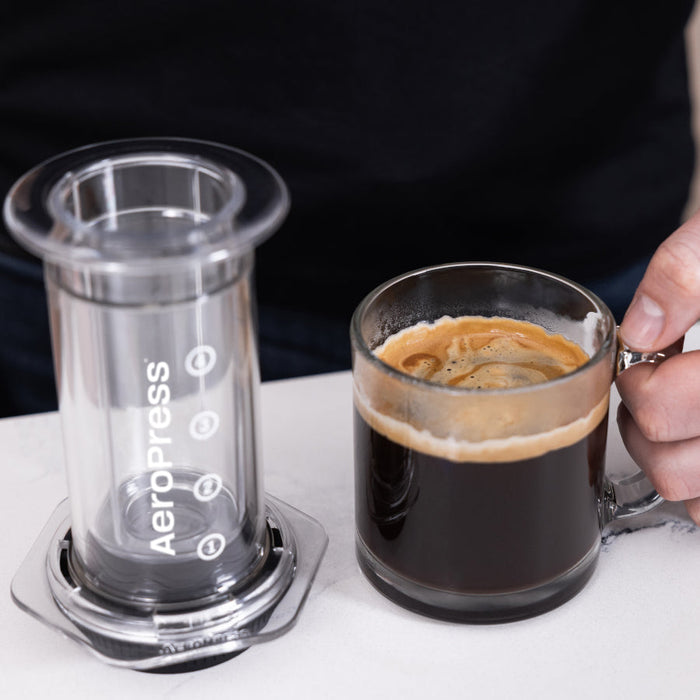 AeroPress coffee maker alongside a glass mug of freshly brewed coffee.
