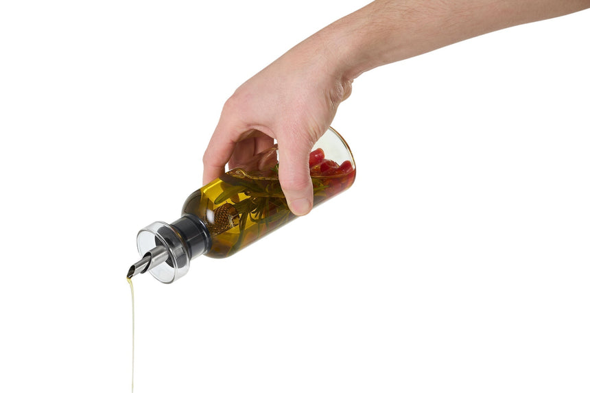 Hand pouring olive oil from a glass bottle with a metal spout.