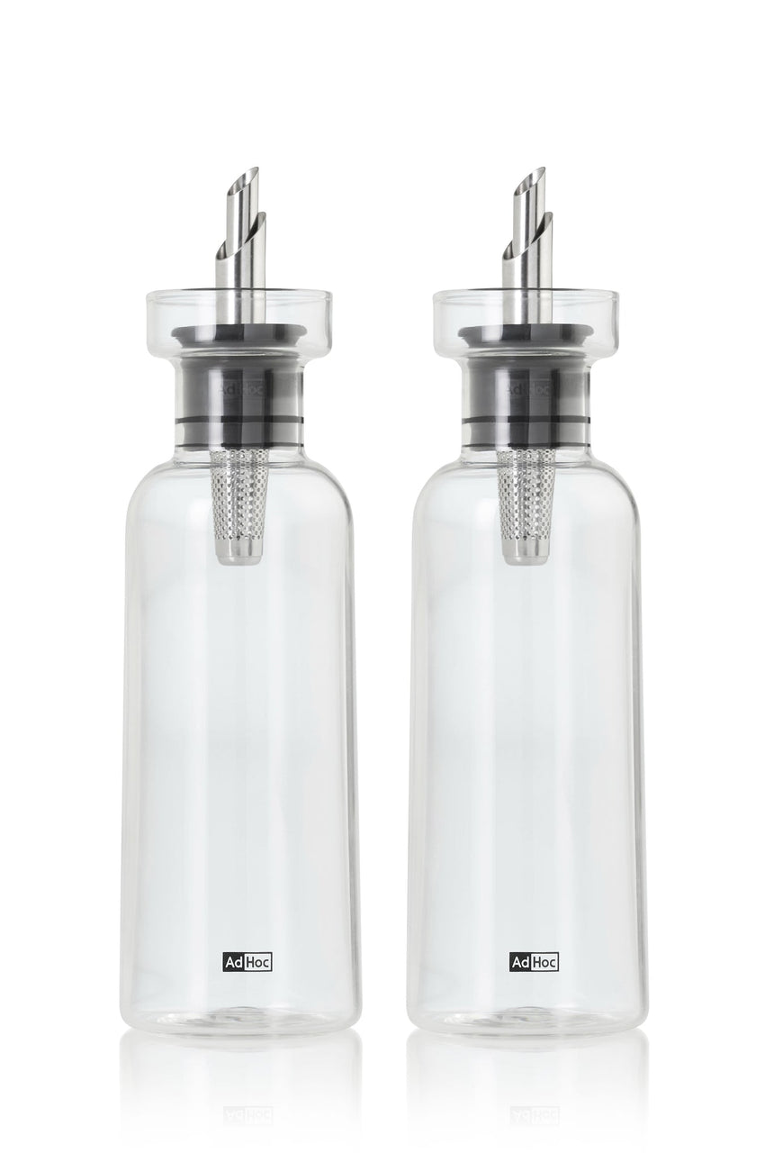Two clear glass oil or vinegar dispensers with metal pouring spouts.