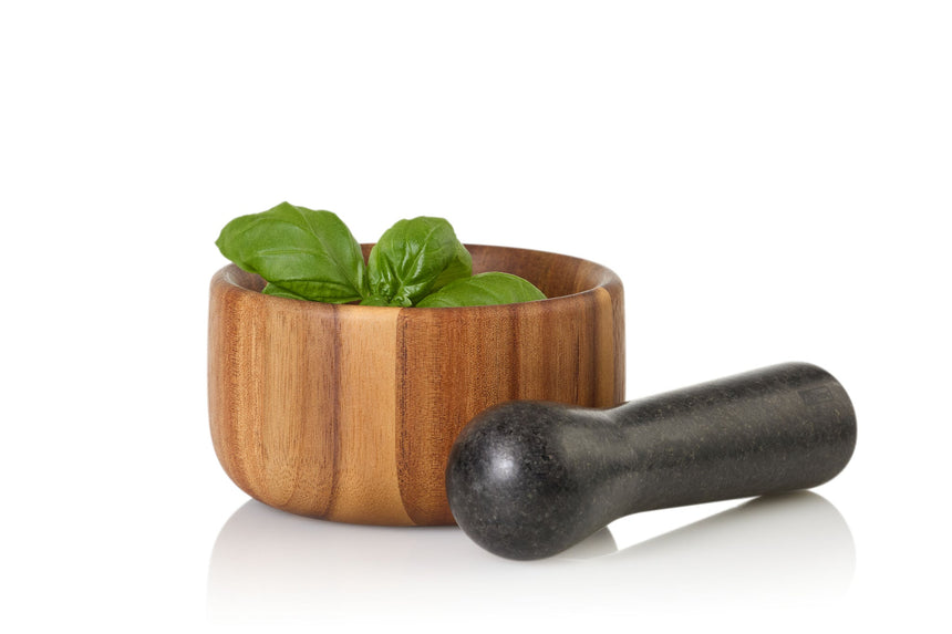 Wooden mortar and pestle with fresh basil leaves.