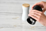 Black pepper grinder being held and used by a hand.