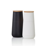 Two tall, cylindrical ceramic containers with wooden lids and vertical ribbed textures, one black and one white.