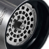 Circular speaker grille with a spiral pattern of square holes.