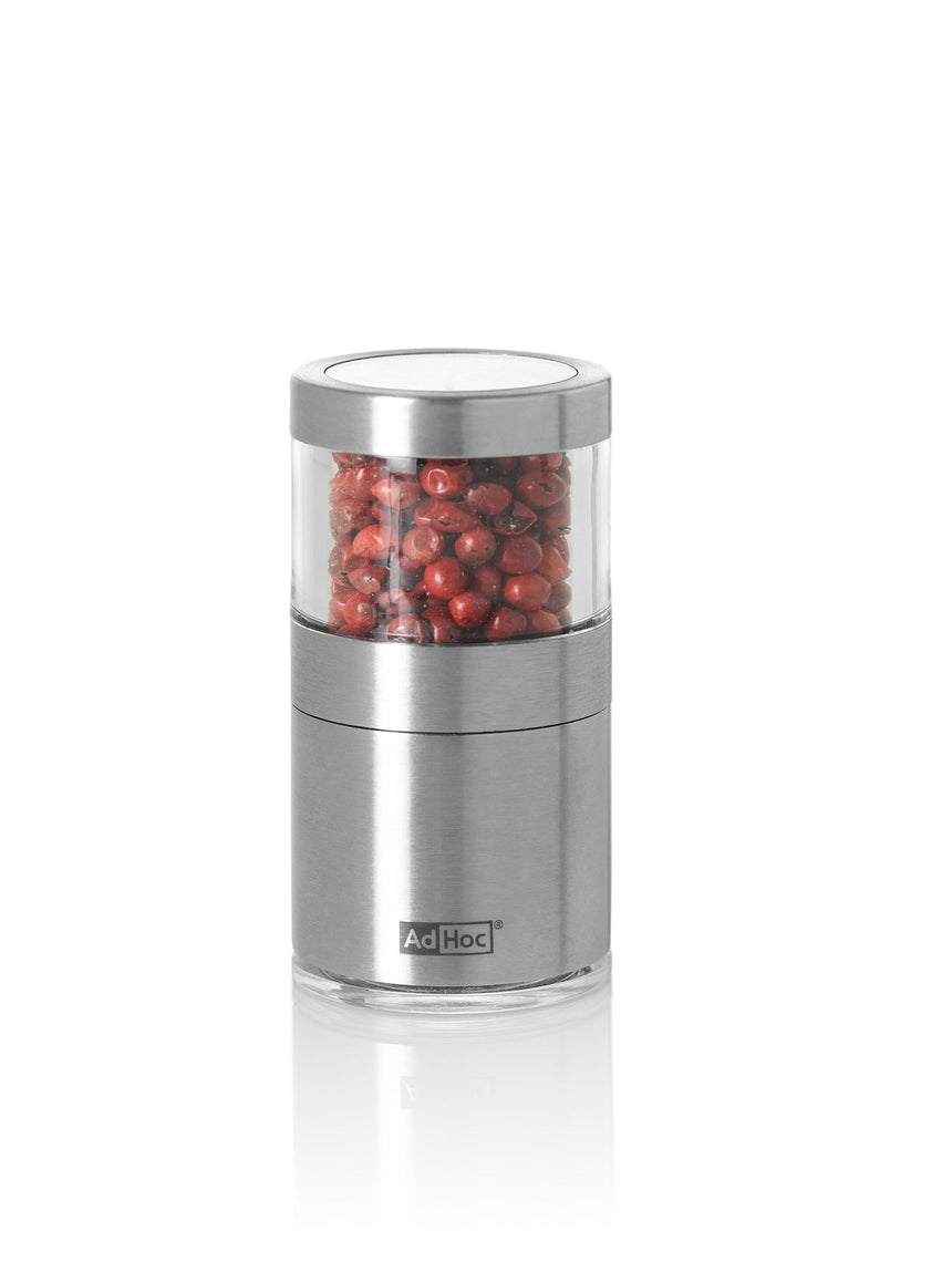 Stainless steel spice grinder containing red peppercorns.