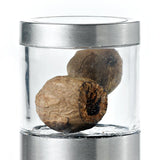 Dried nutmeg seeds in a clear glass container with a metal lid.