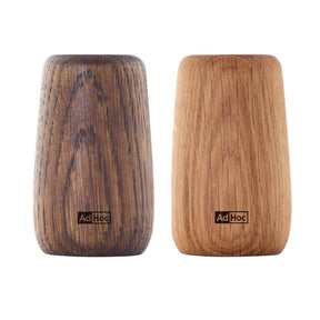 Two wooden salt or pepper shakers with ’AdHoc’ branding, one darker and one lighter in color.