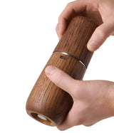 Wooden pepper or spice grinder held by hands.