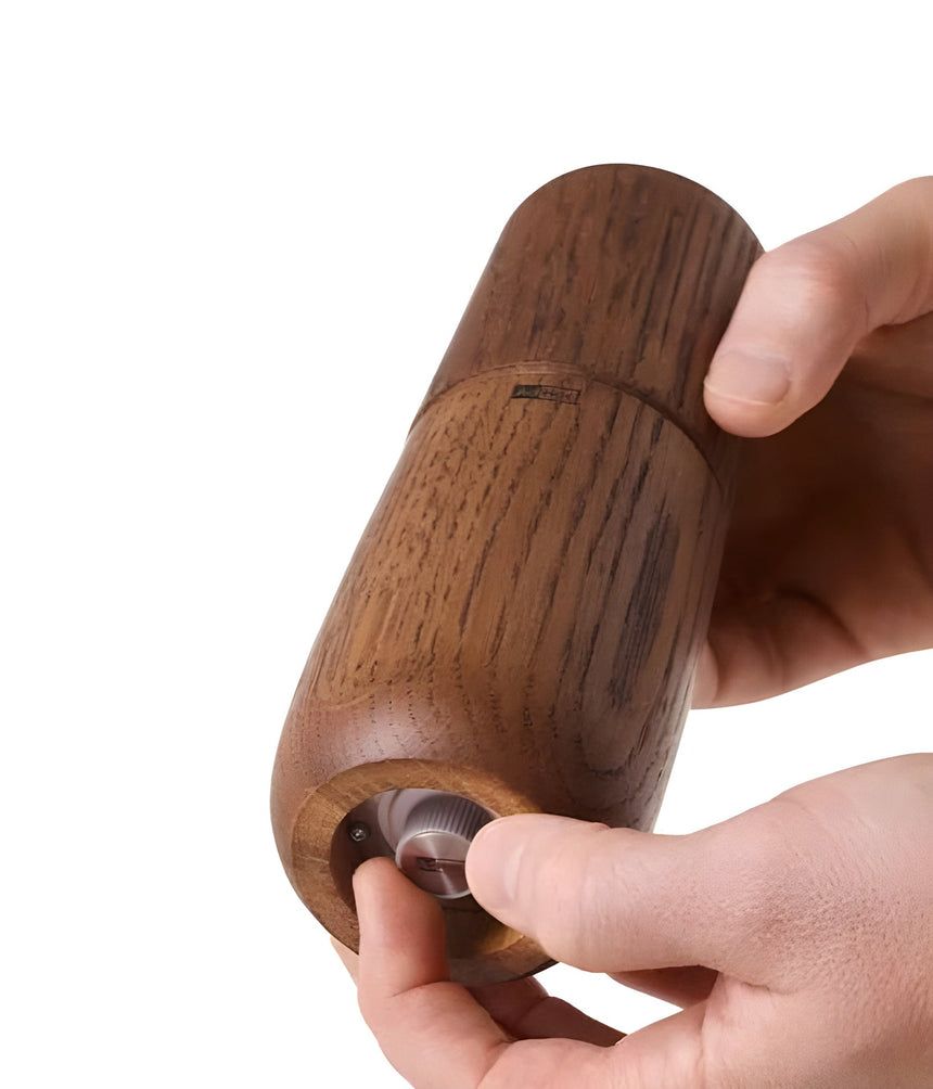 Wooden pepper mill or grinder being held and operated by hands.
