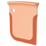 Peach-colored plastic or silicone scraper with a curved edge and a hole for hanging.
