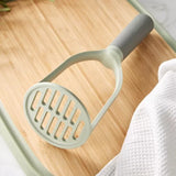Potato masher with a light green handle and slotted circular head.