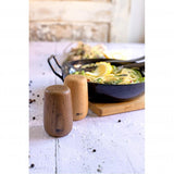 Wooden salt and pepper shakers beside a pan of pasta.
