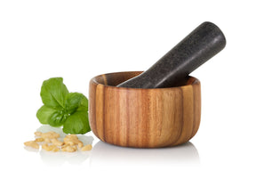 Wooden mortar and pestle with basil leaves and salt crystals beside it.