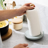 Paper towel roll on a gray stand being torn off by hands.