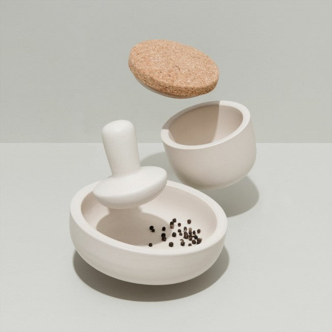 Ceramic mortar and pestle set with a cork lid and small peppercorns inside.