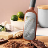 Copper-colored grater with a flat, perforated surface and elongated handle.