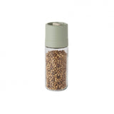 Glass spice grinder filled with light-colored peppercorns and topped with a pale green lid.