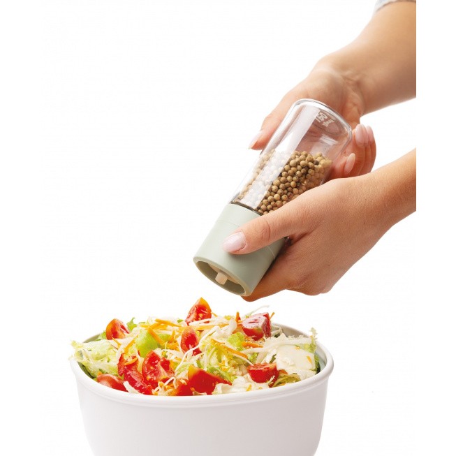 Pepper grinder being used to season a salad in a white bowl.