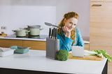 Woman in a blue top sitting at a kitchen counter with cooking ingredients and utensils.