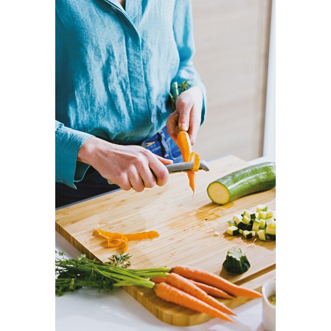 Hands peeling a carrot on a wooden cutting board with various vegetables.