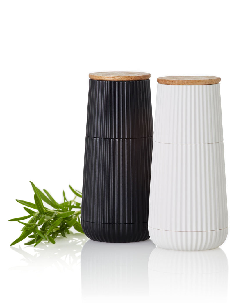 Pair of tall cylindrical ceramic containers with wooden lids, one black and one white, featuring vertical ribbed textures.